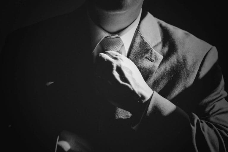 person in a suite adjusting a tie under dramatic lighting
