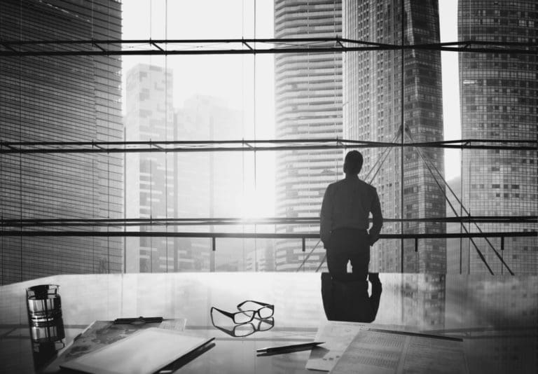 person standing in front of a floor-to-ceiling office window looking at city skyline