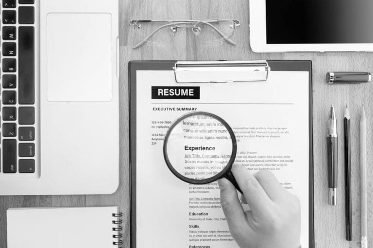 Person's hand holding a magnifying glass over a resume