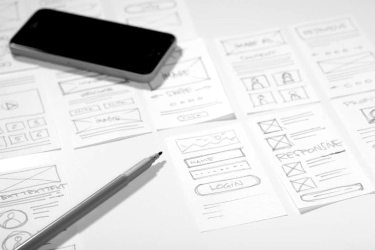website wireframes drawn with pencil on table, with pencil and a smartphone laying on top