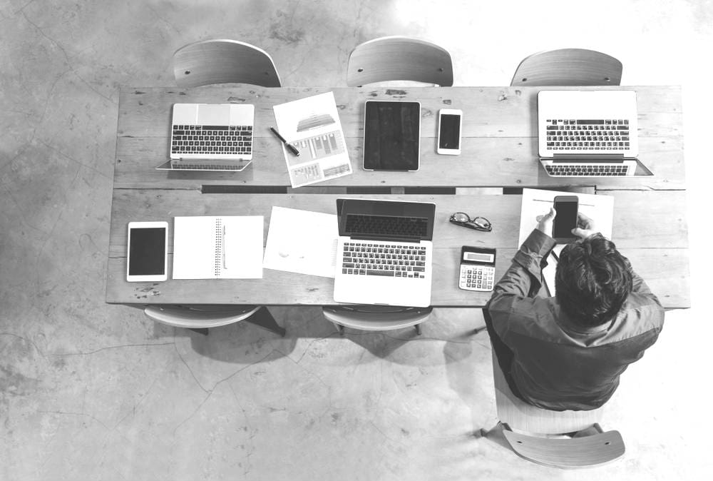 top view of a desk with multiple laptops and devices, one person looking at smartphone
