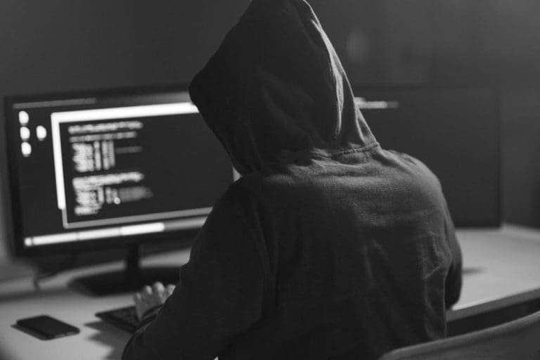 A programmer wearing a hoody faces a computer monitor while writing code